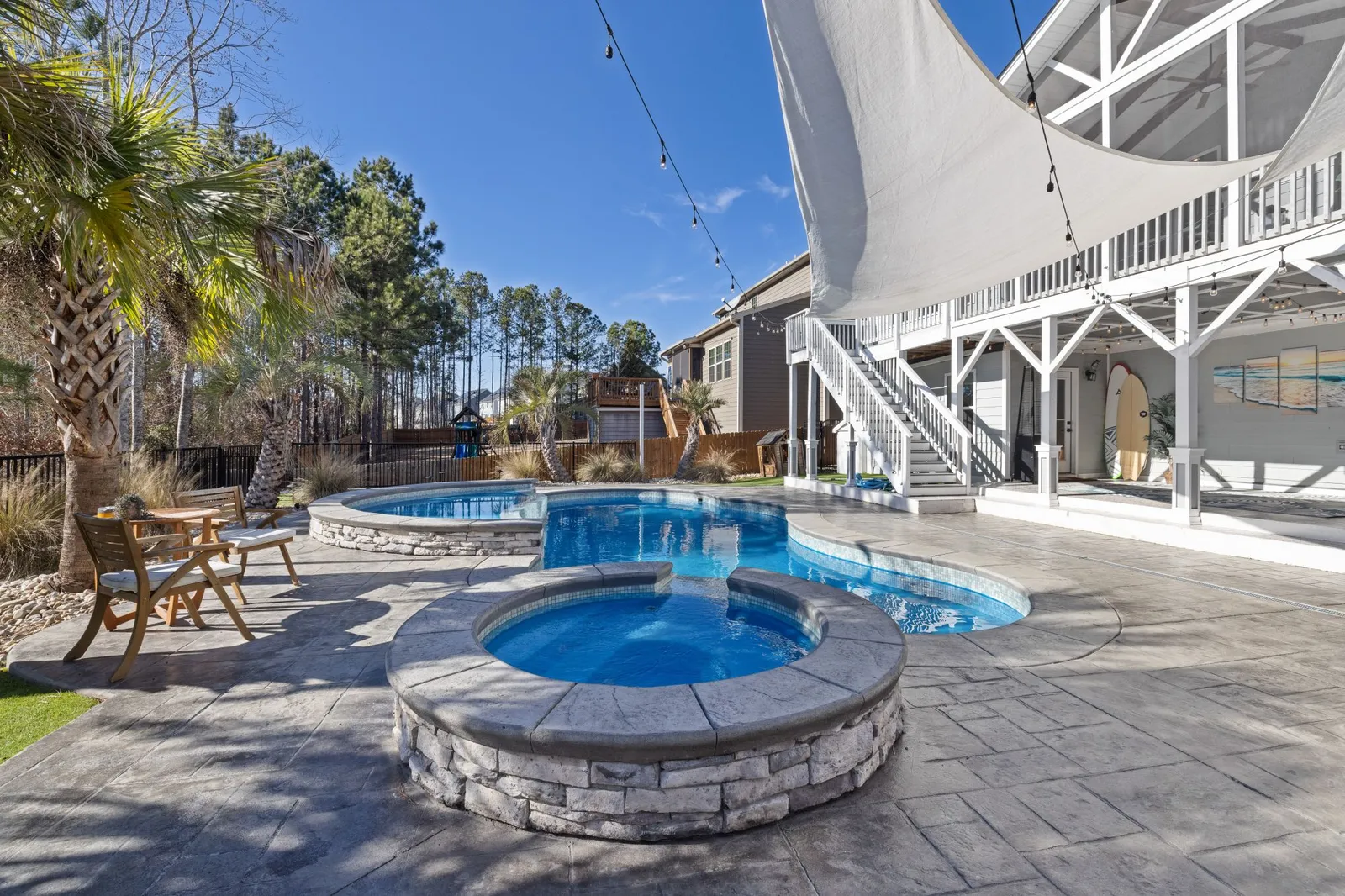Backyard pool and hot tub with a stone patio and palm trees